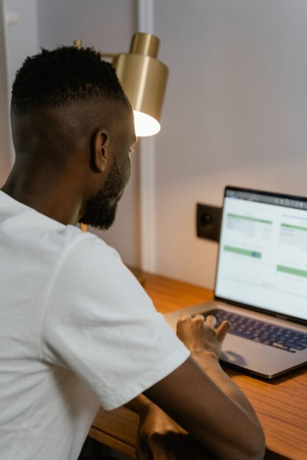 Photo by MART PRODUCTION Adult man using laptop at home desk, focused on screen under warm desk lamp light.